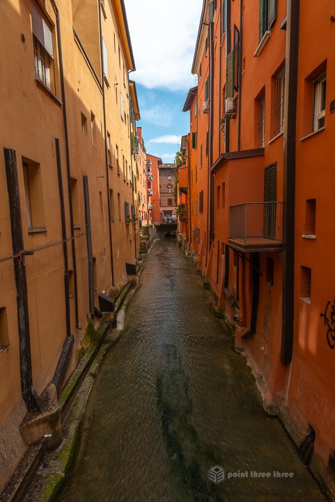Long view of the Reno Canal lined with orange and yellow medieval buildings in Bologna, Italy.