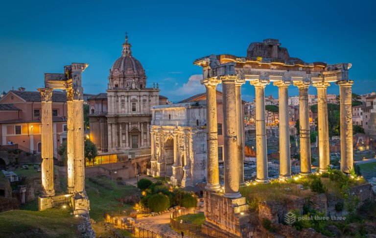 Roman Forum illuminated with golden lights at blue hour showing Temple of Saturn columns and ancient Roman ruins Rome Italy