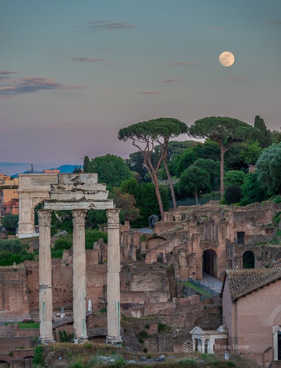 Close-up moon photography over the ancient columns of the Temple of Saturn in the Roman Forum, Rome, Italy, during the blue hour.