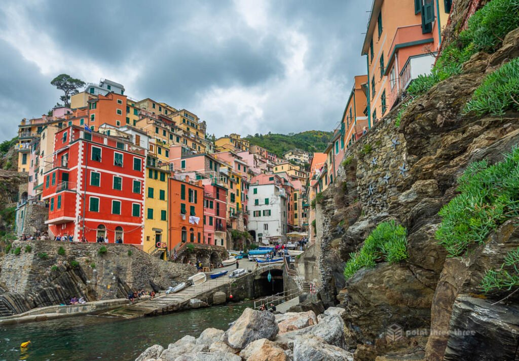 The vibrant red and yellow houses of Riomaggiore village viewed from the rocky marina entrance in Cinque Terre, Italy.