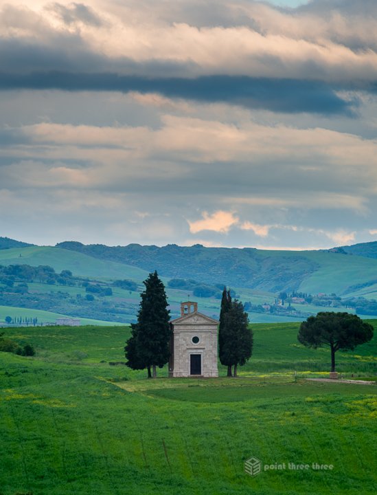 Small stone chapel of Madonna di Vitaleta standing alone in the rolling green hills of the Val d'Orcia region.