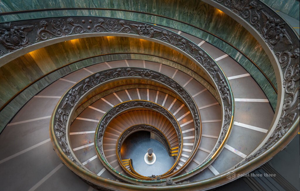 High-angle view of the bronze double helix Bramante Staircase in the Vatican Museums, featuring intricate spiral architecture and ornate railings.