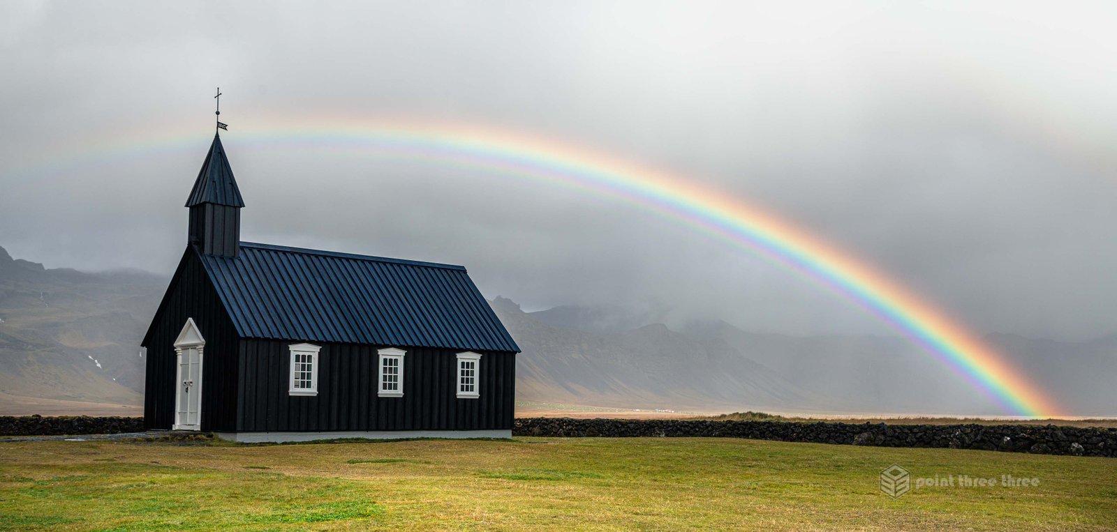 Budir Church in Iceland with vibrant rainbow over top and storm in the background.