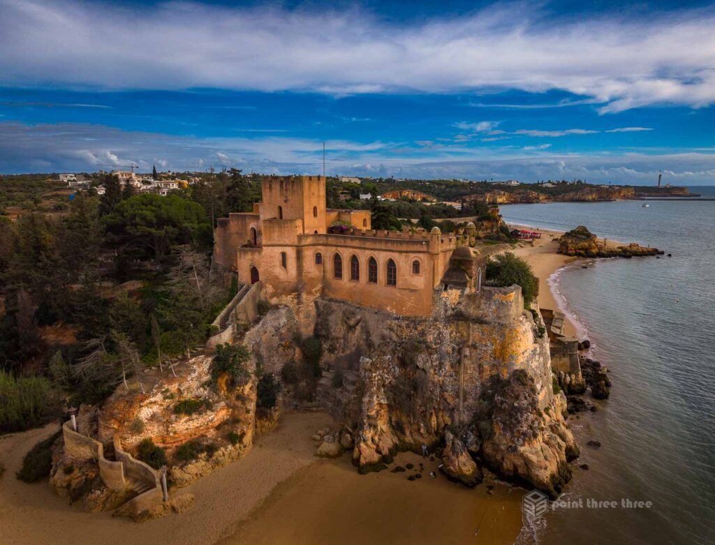 Aerial drone view of the 17th-century Forte de São João do Arade perched on limestone cliffs above the Rio Arade estuary at Ferragudo, Algarve, Portugal, with golden morning light on the battlements.